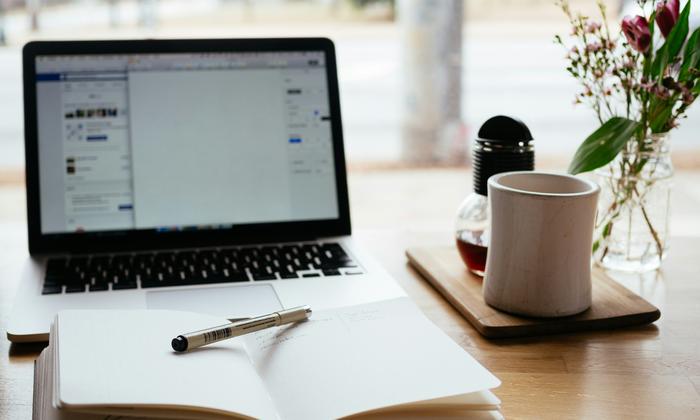 An open notebook and pen next to a laptop on a desk